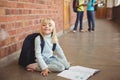 Cute pupil kneeling over notepad at corridor