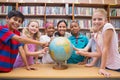 Cute pupils and teacher looking at globe in library Royalty Free Stock Photo