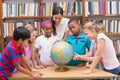 Cute pupils and teacher looking at globe in library Royalty Free Stock Photo