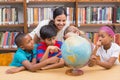 Cute pupils and teacher looking at globe in library Royalty Free Stock Photo