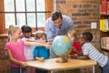 Cute pupils and teacher looking at globe in library Royalty Free Stock Photo