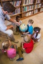 Cute pupils and teacher looking at globe in library Royalty Free Stock Photo