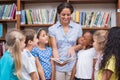 Cute pupils and teacher reading book in library