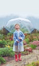 Cute, raincoat and rain for umbrella, child and outdoor with smile for winter, sky and safety footwear. Happiness, shoes Royalty Free Stock Photo