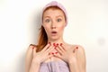 Cute red-haired girl is standing on a white background in a towel looking shockingly at the camera, clutching her hands Royalty Free Stock Photo