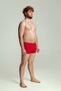 Cute red-headed man in red swimming shorts posing isolated on gray studio background. Concept of sport, humor and body