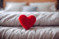 Cute red heart on a white bed, blurred background.