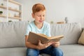 Cute redhead boy sitting at home, reading book Royalty Free Stock Photo