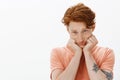 Cute redhead european man with freckles on face, leaning head on hands and gazing with gloomy upset expression at camera