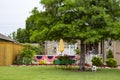 Cute rock house decorated for 4th of July bunting and flags with nice landscaping and a huge walnut tree and woman on porch unfold