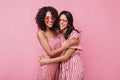 Cute romantic girls hug each other in friendly way. Ladies in pink sunglasses laughing on isolated