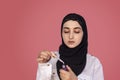 Cute 20s female putting lipstick with a brush. Beautiful Persian woman in hijab doing make-up applying lipstick on her lips Royalty Free Stock Photo