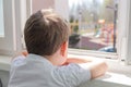 Cute sad boy of four years old is sitting on the balcony and looking out the window at the playground. Self-isolation quarantine Royalty Free Stock Photo