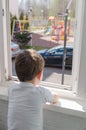 Cute sad boy of four years old is sitting on the balcony and looking out the window at the playground. Self-isolation quarantine Royalty Free Stock Photo