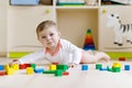 Cute sad crying baby playing with colorful wooden blocks toys. New born child, little girl looking at the camera and Royalty Free Stock Photo