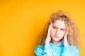 Cute sad girl with blond curly hair in a blue sweater puts her hands on her face Royalty Free Stock Photo