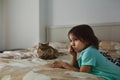 Cute sad little girl watching TV alone in the bedroom with a cat lying on bed Royalty Free Stock Photo