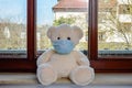 Teddy bear with protective medical mask in quarantine near the window. Stay home concept Royalty Free Stock Photo