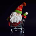 Cute Santa Claus toy, sitting in red shopping cart. Christmas sale or New Year concept, isolated on black background Royalty Free Stock Photo