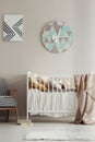 Cute, scandi bedroom interior for a child with a white crib, pastel wall and a round clock. Real photo