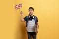 Cute school boy showing flag of UK, yellow background Royalty Free Stock Photo