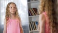 Cute school girl in pink dress standing in front of mirror, childhood fashion Royalty Free Stock Photo