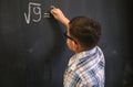 Cute schoolboy boy solves a math problem on a black blackboard