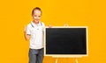 A cute schoolboy in a white T-shirt on a yellow background near the board smiles and shows his thumb raised up. Banner. A place