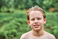 Cute schooler with wet blond hair stands against lush trees