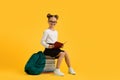 Cute Schoolgirl In Eyeglasses Sitting On Pile Of Books Over Yellow Background Royalty Free Stock Photo