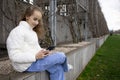 A cute schoolgirl girl is sitting on a bench in a spring park and watching videos or messages on her smartphone. Modern Royalty Free Stock Photo
