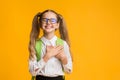 Cute schoolgirl posing putting hands on heart on yellow background