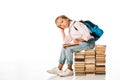 cute schoolkid sitting on books and looking at camera on white.