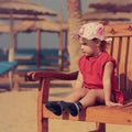 Cute serious kid girl in hat sitting on the bench