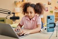 Cute serious schoolgirl looking at laptop screen while recording new podcast Royalty Free Stock Photo