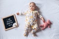 7 Seven months old baby girl laying down on white background with letter board and teddy bear. Flat lay composition.