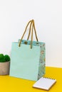 Cute shopping bag on yellow desktop, in front of white wall with a little note pad