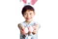 Cute short haired smiling little child with blurred face wearing bunny ears on Easter day with two painted pink eggs in hands Royalty Free Stock Photo