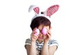 Cute short haired smiling little child wearing bunny ears on Easter day with two painted pink eggs in hands in front of face Royalty Free Stock Photo