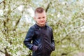 Cute short-trimmed seven-year-old boy in black leather jacket during garden bloom