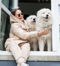 Cute shot of the two dogs breed samoyed sitting on the windowsill together with their beautiful adorable brunette owner.