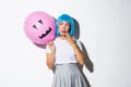 Cute and silly asian girl in blue wig, celebrating halloween, looking surprised at balloon with scary face Royalty Free Stock Photo