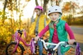 Cute sisters riding bikes in a city park on sunny autumn day. Active family leisure with kids. Children wearing safety hemet while Royalty Free Stock Photo