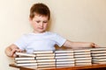 A cute six-year-old boy sits at a Desk and puts books on stacks Royalty Free Stock Photo