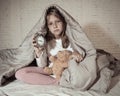 Little girl sitting on bed with teddy bear and alarm clock sleepless at night feeling restless