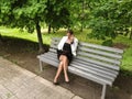 Cute slender woman in a business suit sits on a bench in the park with a laptop and speaks by phone. An adult girl in glasses