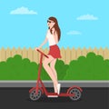 Cute slender young girl in glasses, a T-shirt and a skirt coquettishly touches brown hair. Standing by the scooter holding the