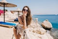 Cute slim tanned girl in sunglasses looking with interest, while resting outside on sea resort. Portrait of lovely young Royalty Free Stock Photo