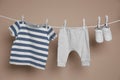 Cute small baby shoes and clothes hanging on washing line against brown background Royalty Free Stock Photo