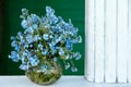 Cute small bouquet of blue garden forget me not flowers in round glass vase on old green wooden background